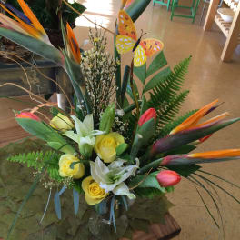 Tropical bouquet with yellow roses, white lilies, and bird-of-paradise flowers in a glass vase