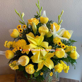Tall yellow floral arrangement with lilies, roses, and daisies in a container