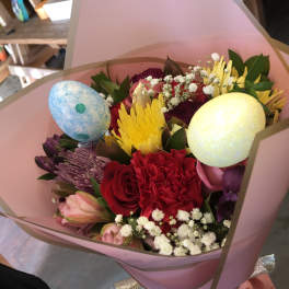 Hand-tied bouquet of bright mixed flowers with decorative pastel eggs wrapped in pink paper