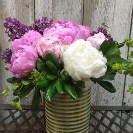 Pink and white peonies in a striped ceramic vase with purple lilac accents