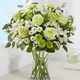 Green and white bouquet of roses, carnations, and daisies in a clear glass vase