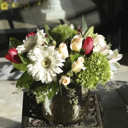 Bouquet of white daisies, pale roses, and red tulips in a glass vase