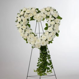 White floral heart wreath on a black stand with trailing greenery