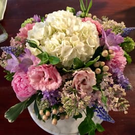 Round bouquet of white, pink, and purple flowers in a low white vase