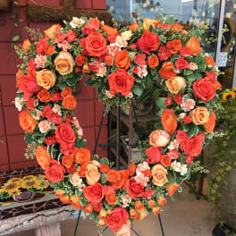 Heart-shaped floral wreath of orange and red roses on a stand