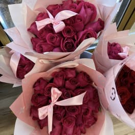 Bouquets of deep pink roses wrapped in pale pink paper with satin bows