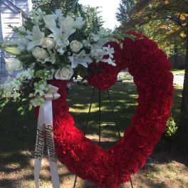 Heart-shaped floral wreath with red and white flowers on an outdoor stand