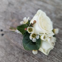 White rose boutonniere with small white blossoms and dark green leaves