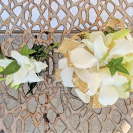 Two white floral boutonnieres with green accents and gold ribbon