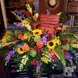 Large colorful floral arrangement with sunflowers and roses around a wooden chair
