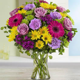 Mixed bouquet of pink, purple, and yellow flowers in a clear glass vase