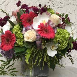 Mixed bouquet with pink gerbera daisies, white orchids, and cream roses in a ribbed vase