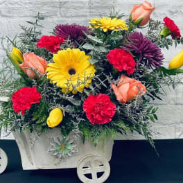 Mixed bouquet in a white decorative cart with yellow, pink, and peach blooms