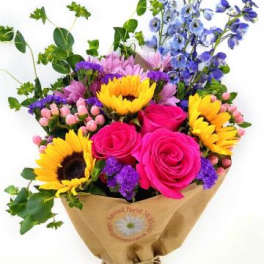 Bouquet of pink roses, sunflowers, and blue flowers wrapped in brown paper