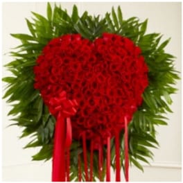 Heart-shaped red rose arrangement with a red ribbon and green foliage