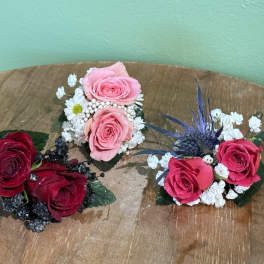 Three small rose corsages with baby's breath on a wooden surface