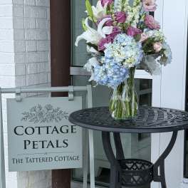 Mixed bouquet in a clear glass vase with lilies, roses, and blue hydrangeas