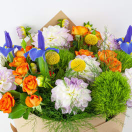 Bouquet of orange roses, white dahlias, and blue irises in kraft paper