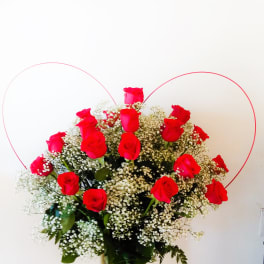 Red roses arranged in a glass vase with baby's breath and heart-shaped wire accents.