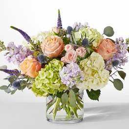 Pastel bouquet of roses, hydrangeas, and purple spikes in a clear glass vase