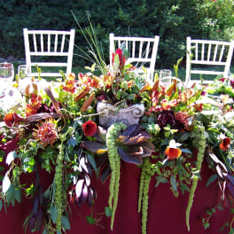 Long floral table centerpiece with burgundy, orange, and green blooms