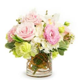 Low arrangement of pink roses and mixed pastel flowers in a clear glass vase with curly branches.