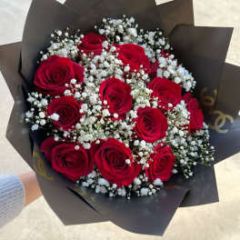 Handheld bouquet of red roses and white filler flowers wrapped in dark black paper