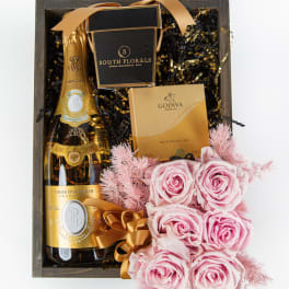 Wooden gift box with champagne, gold chocolate box, and pink roses tied with ribbon