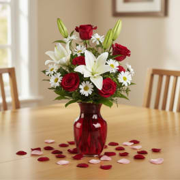 Red roses and white lilies in a red glass vase with scattered petals