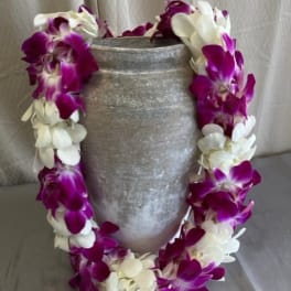 Purple and white orchid lei draped over a gray vase