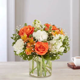 Orange roses and white flowers arranged in a clear glass vase