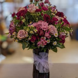 Mixed pink and purple flower arrangement in a dark vase with a lavender bow