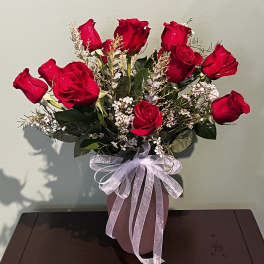 Red roses arranged in a pink vase with a sheer ribbon bow