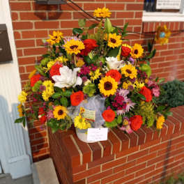 Large mixed bouquet of sunflowers, roses, and lilies in a white container