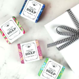 Four wrapped soap bars beside a white gift box with a black ribbon