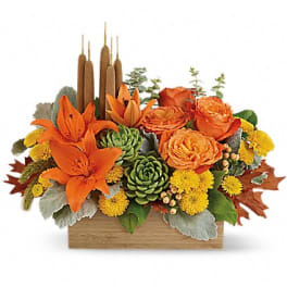 Orange flowers and succulents in a wooden box with tall brown candles
