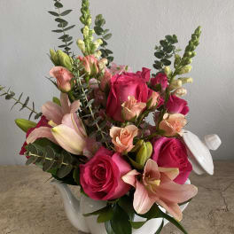 Pink roses and lilies arranged in a white ceramic teapot.