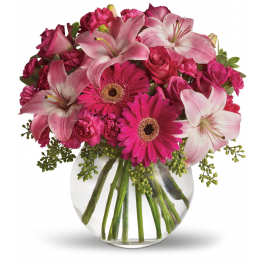 Pink lilies, roses, and gerbera daisies arranged in a clear glass vase