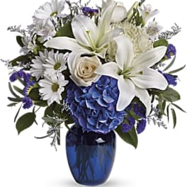 White lilies, daisies, and blue hydrangea in a blue glass vase