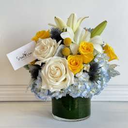 Bouquet of white roses, yellow roses, lilies, and blue hydrangeas in a glass vase