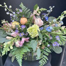 Pastel garden-style flower arrangement in a clear glass vase against a dark background