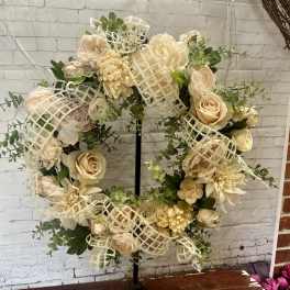Cream floral wreath on a black stand with burlap ribbon accents