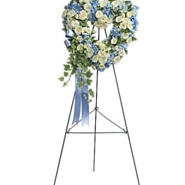 Heart-shaped floral wreath on a standing easel with blue and white flowers