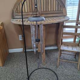 Black metal wind chime hanging in front of a wooden table and chair