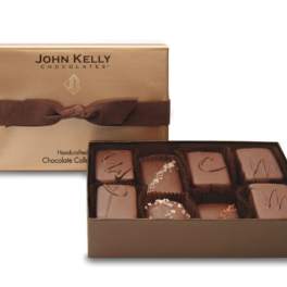 Gold gift box of assorted gourmet chocolates with the lid tied in a wide brown ribbon.