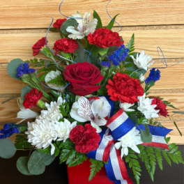 Red, white, and blue floral arrangement in a red container with ribbon
