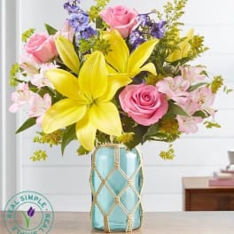 Bouquet of pink roses, yellow lilies, and purple flowers in a blue vase