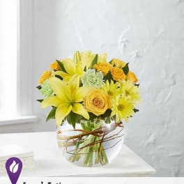 Yellow lilies, roses, and daisies arranged in a clear glass vase