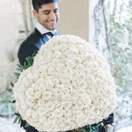 Man holding a large round bouquet of white roses