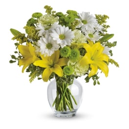 Yellow lilies, white daisies, and green blooms arranged in a clear glass vase